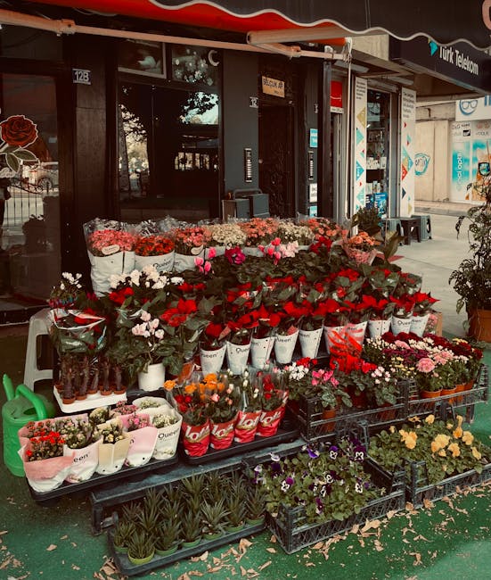 An outdoor display of fresh flowers in front of a flower shop with the signage 'Blackwall same day flowers delivery East India Dock Road.' The arrangement includes various vibrant blooms such as red r